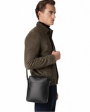 Man wearing a brown jacket with a green crossbody bag on a white background
